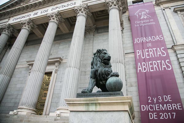 Fotografía de la fachada del Congreso de los Diputados en Madrid, en la que se ve una estatua de bronce de un león y las columnas que hay justo antes de la puerta de entrada. También hay un estandarte en el que se lee: Congreso de los Diputados. Jornada de Puertas Abiertas. 2 y 3 de diciembre de 2017